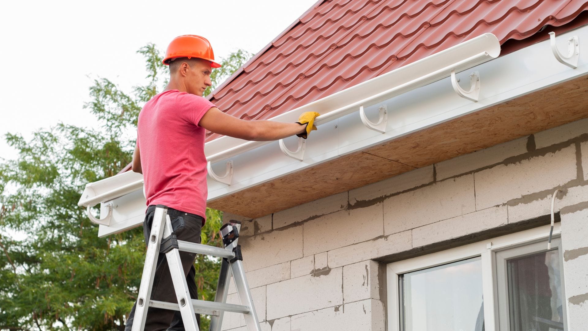 Installer fitting a seamless gutter under a roof edge