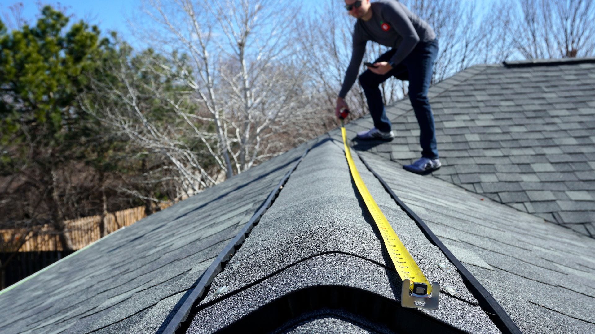Roofer taking measurements along a ridge during an inspection